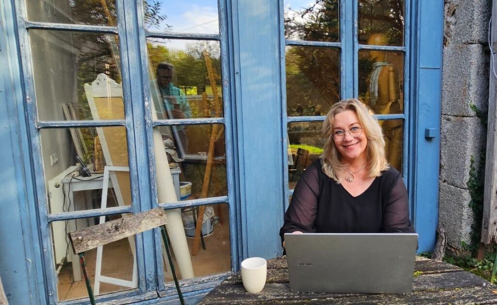 Marion zit buiten achter haar laptop met een kop koffie