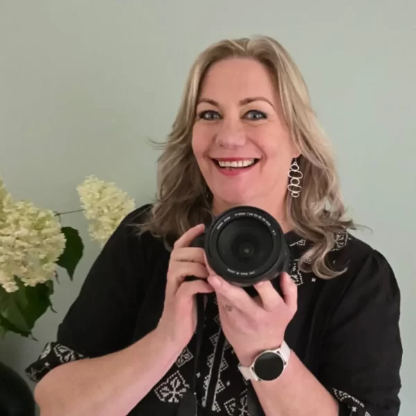 Professionele branding fotograaf helpt ondernemers met een krachtige visuele identiteit. Ze houdt een cameralens vast en lacht, klaar om authentieke beelden te creëren.