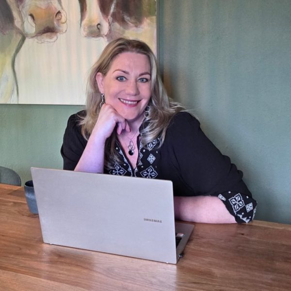 Vrouw met blond haar glimlacht achter laptop aan houten tafel, werkt aan strategie voor startende ondernemer tijdens het traject Van Passie naar Plan bij The SalesCreator